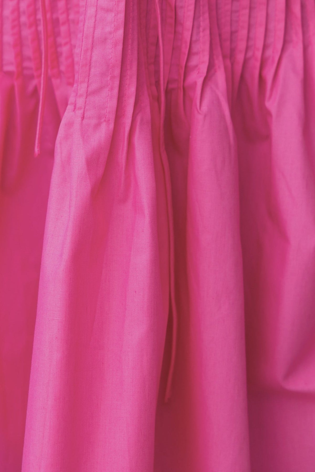 Close-up of the pleated fabric and tie detail of the Zayna Dress in vibrant pink.