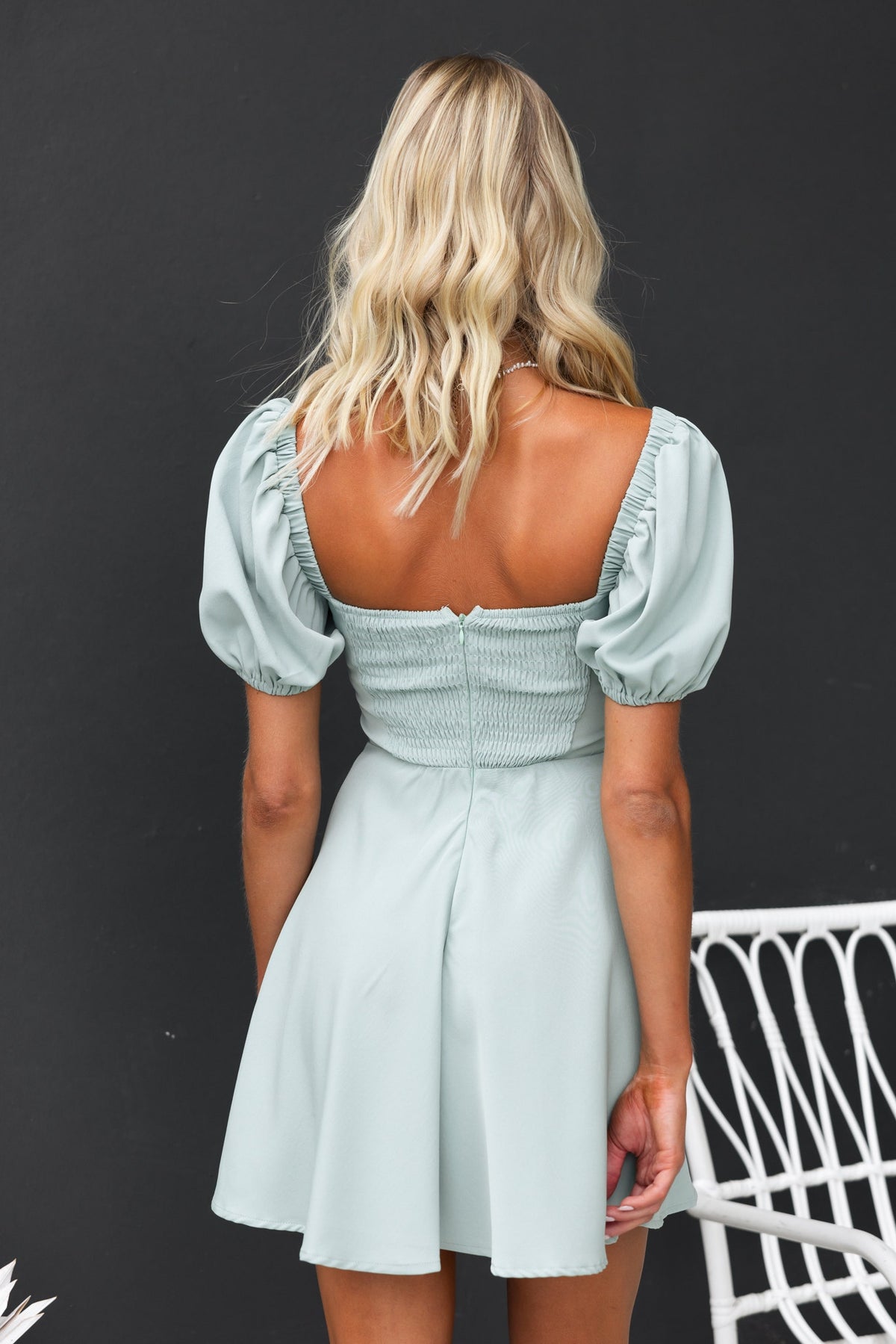 Back view of the Nonny Dress in light green with elastic sleeves and lace details, featuring a fitted bodice and flared skirt.