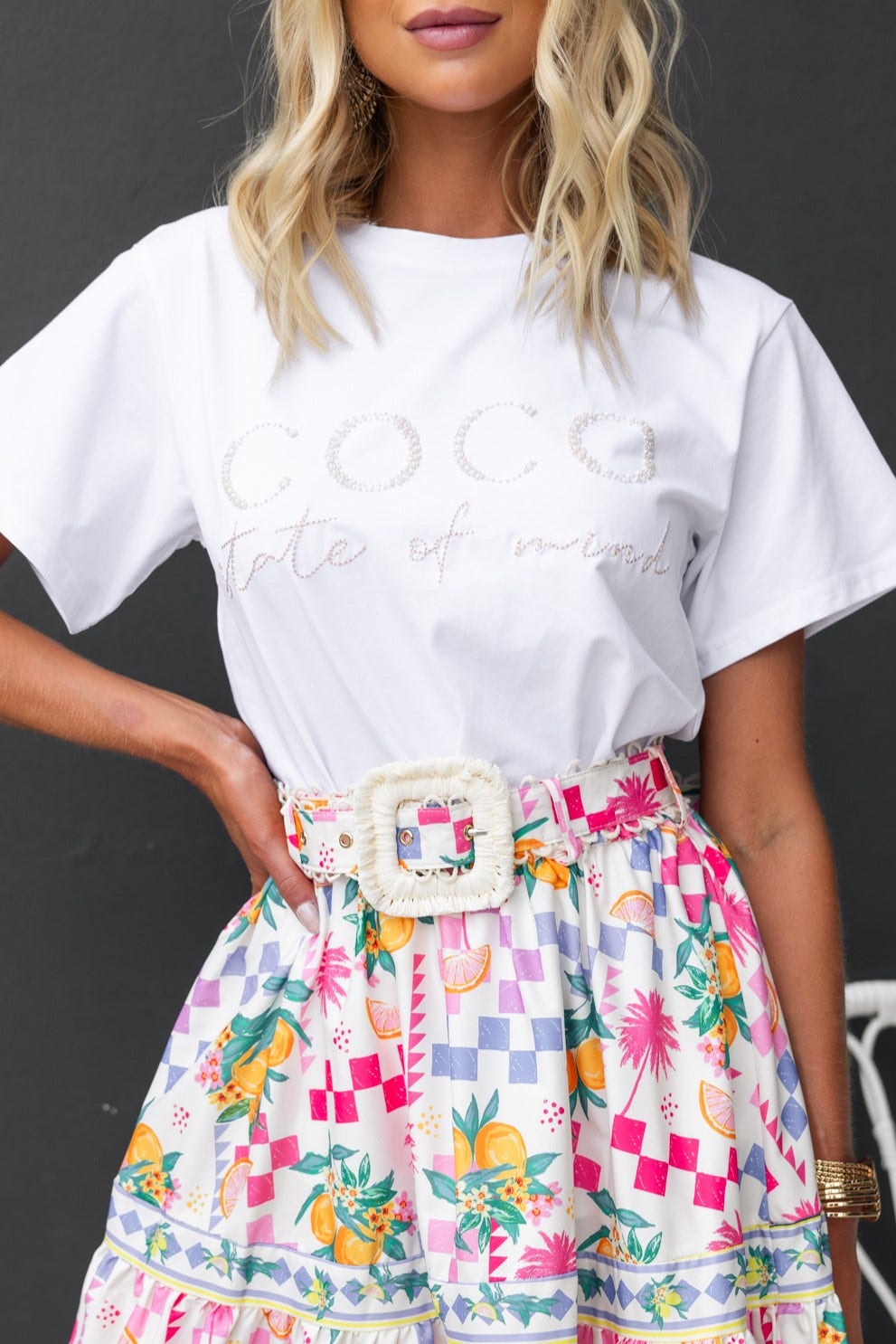 Model wearing Margot Tee with 'Coco state of mind' print, paired with a colorful floral skirt and statement belt.