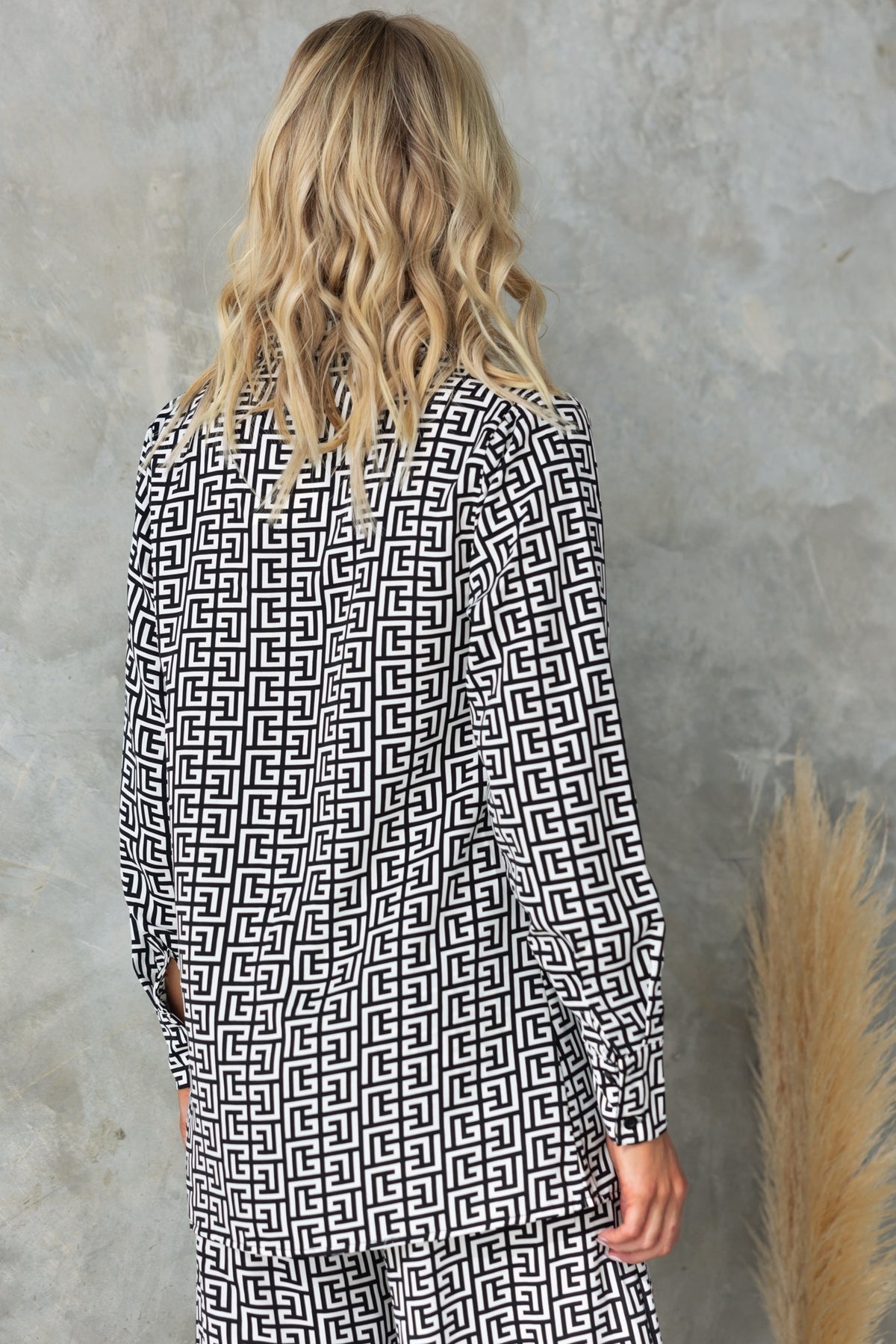 Back view of a woman wearing a black and white abstract printed Steffy shirt against a textured background.