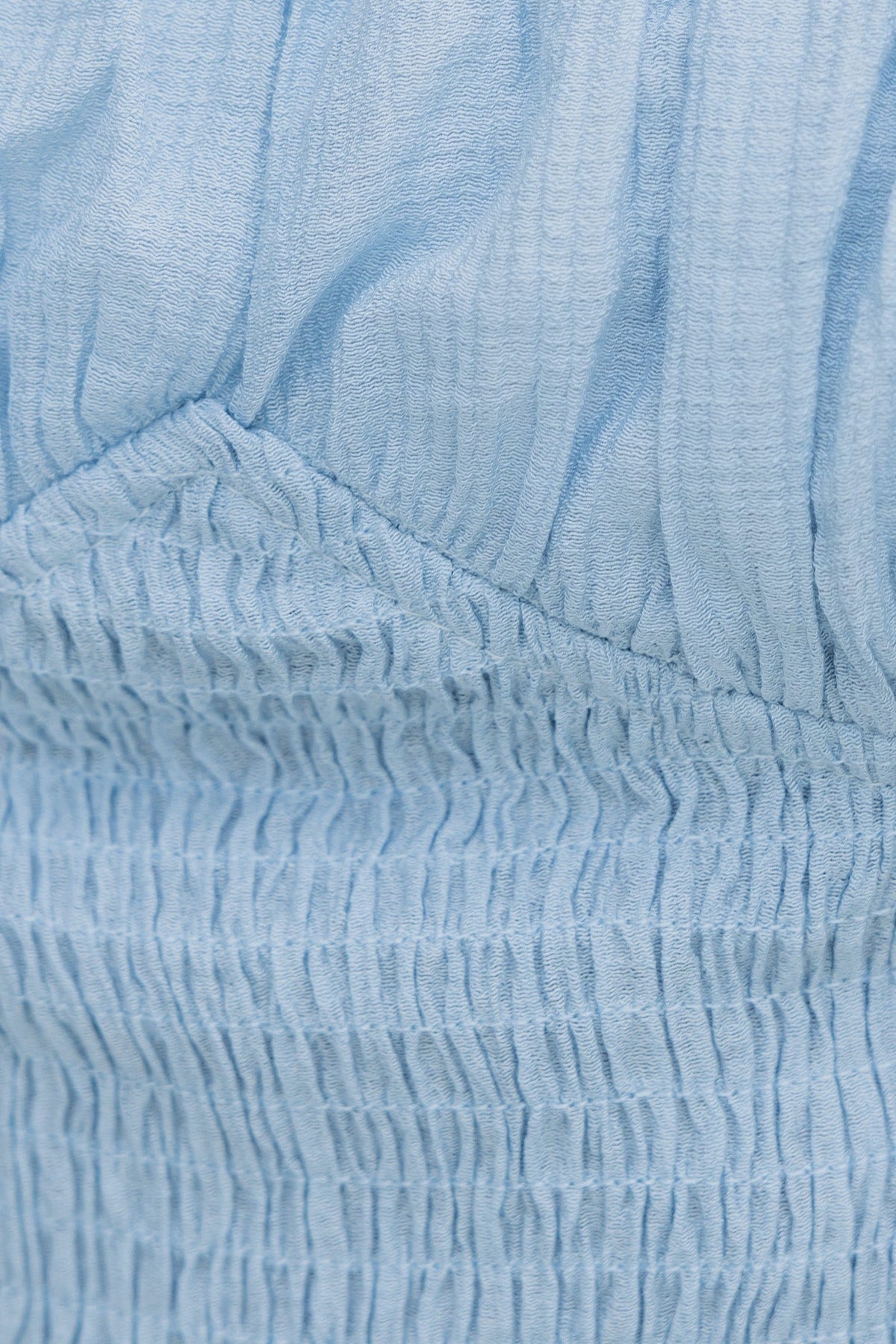 Close-up of light blue linen-look fabric with elastic bodice and smocking detail, showcasing texture and softness.