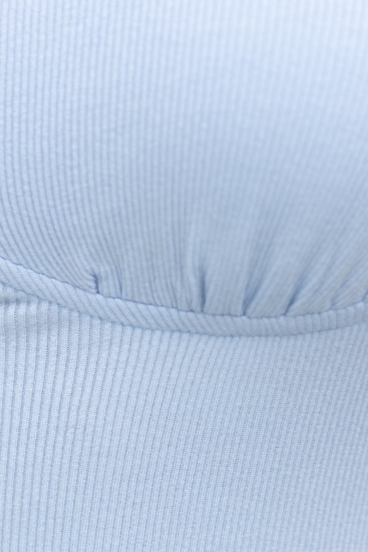 Close-up of the ribbed fabric of the Rhodes Bodysuit in light blue, showcasing its texture and gathered design.