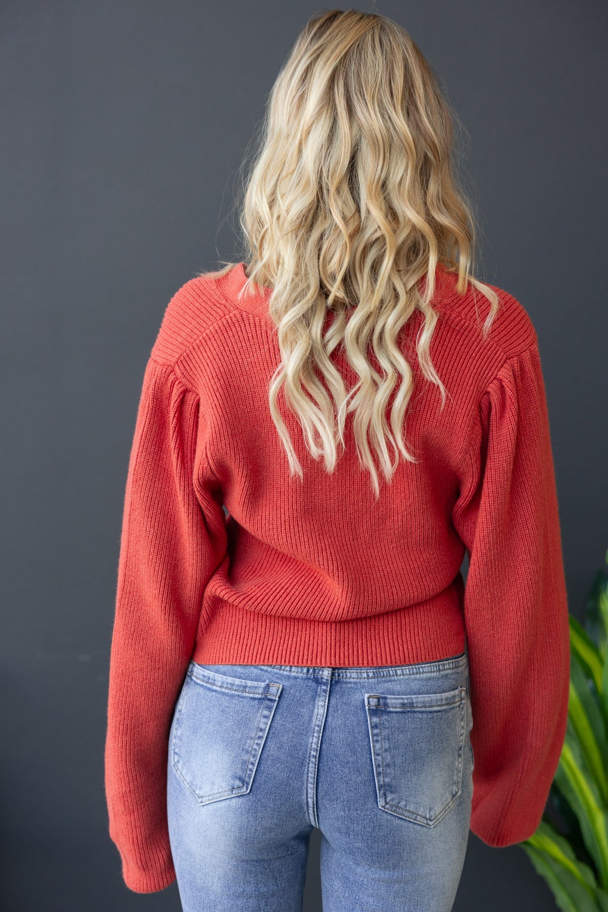 Back view of a woman in a red Modalla cardigan paired with light blue jeans, showcasing a relaxed fit and soft knit texture.