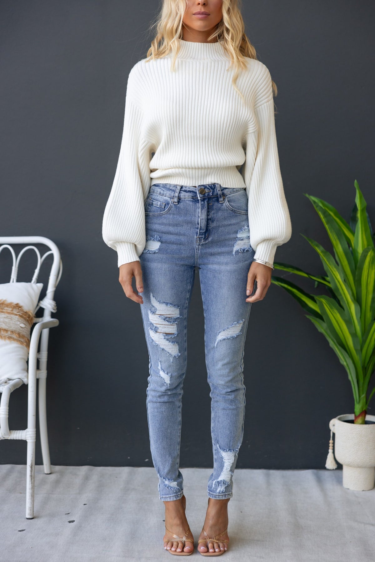 Model wearing a white ribbed Sola Jumper with wide sleeves, paired with ripped blue jeans against a neutral backdrop.