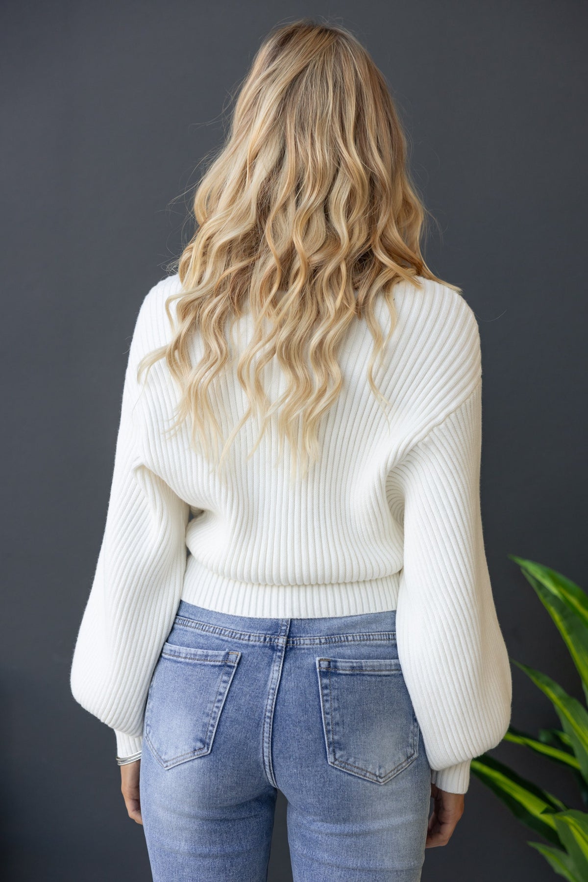 Back view of a model wearing a stylish white ribbed Sola Jumper paired with light blue jeans.