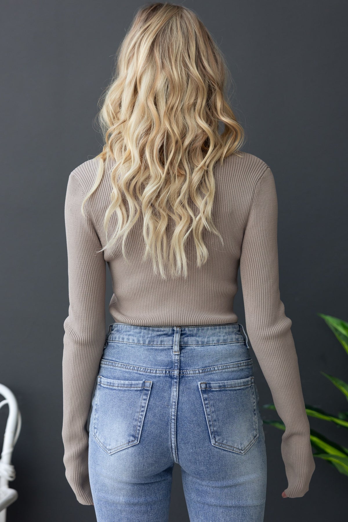 Back view of a woman wearing a ribbed beige top with long sleeves and high-waisted blue jeans.