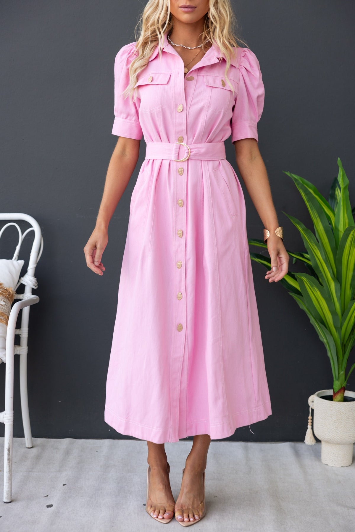 Pink denim maxi dress with button-up front, removable belt, and faux pockets, styled with stylish sandals.