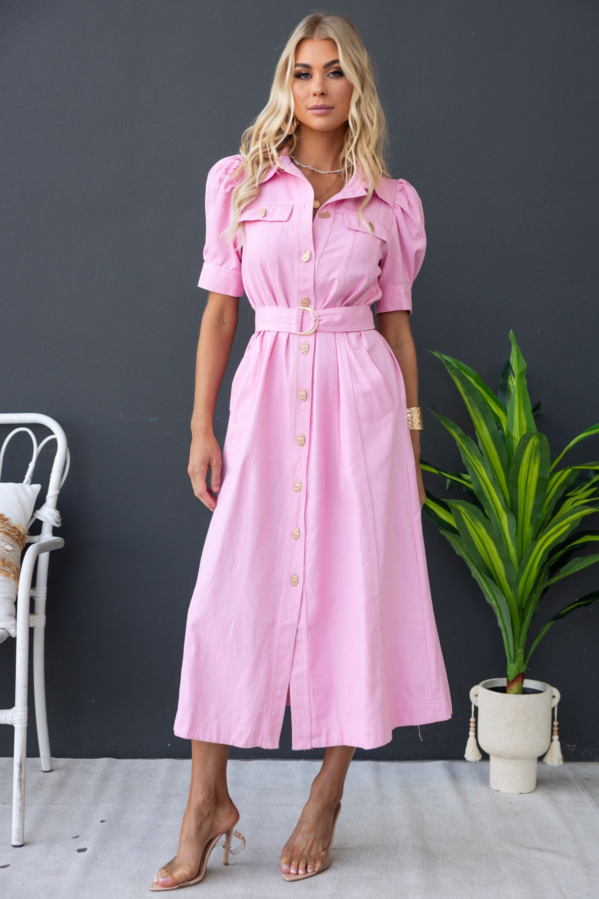 Model wearing a pink denim maxi dress with buttons, collar, and removable belt in a stylish setting.