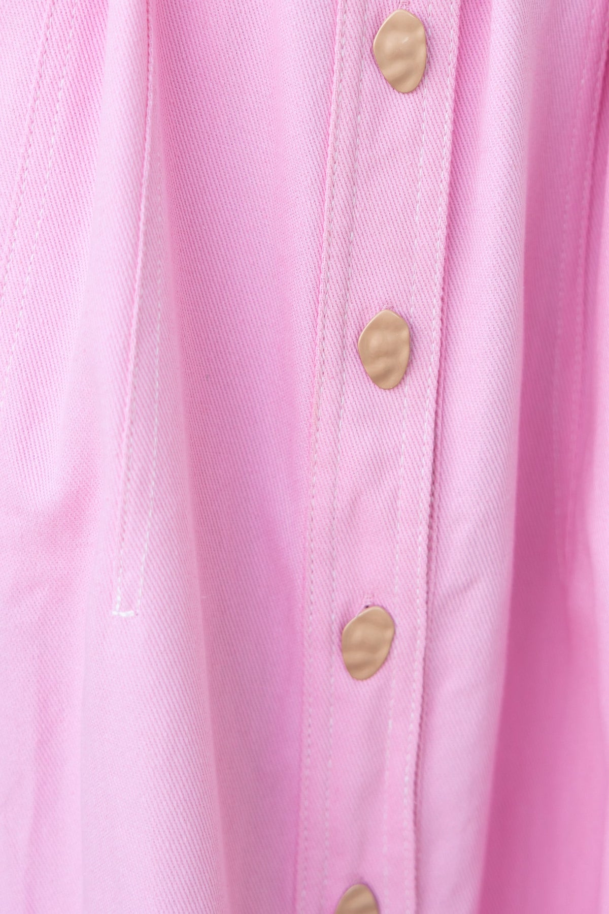 Close-up of berry denim maxi dress buttons, showcasing pink fabric and brass button details.