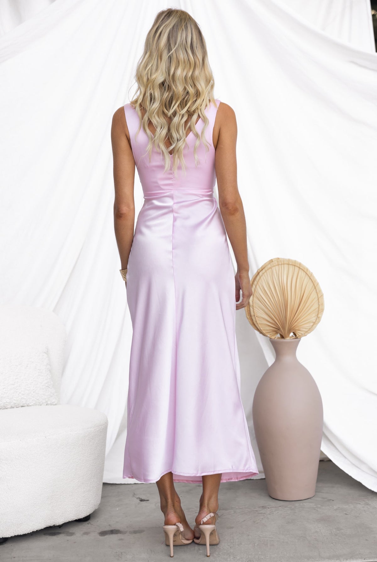 Back view of Aerida Midi Dress in soft pink with satin finish, styled with elegant accessories.