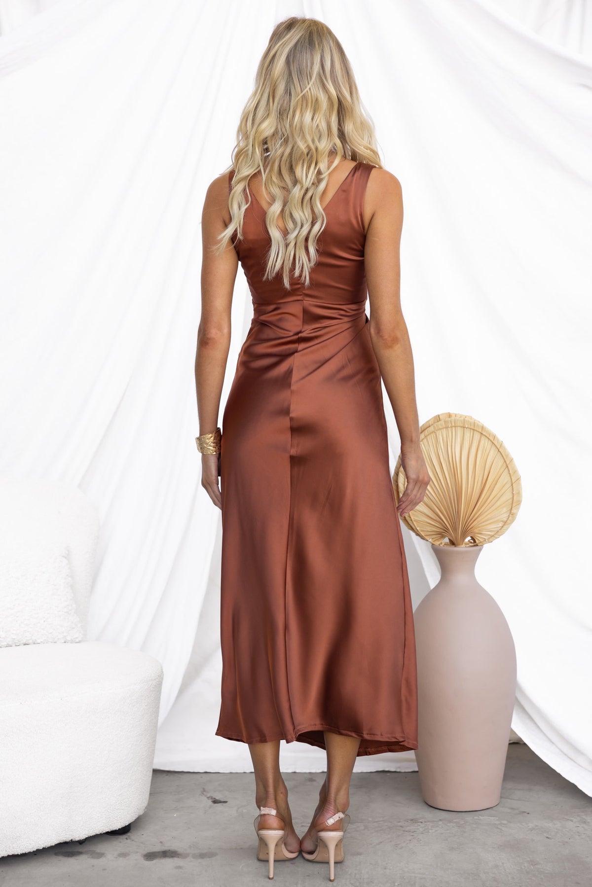 Back view of a model wearing the Aerida Midi Dress in rust satin, styled with a minimalistic decor.