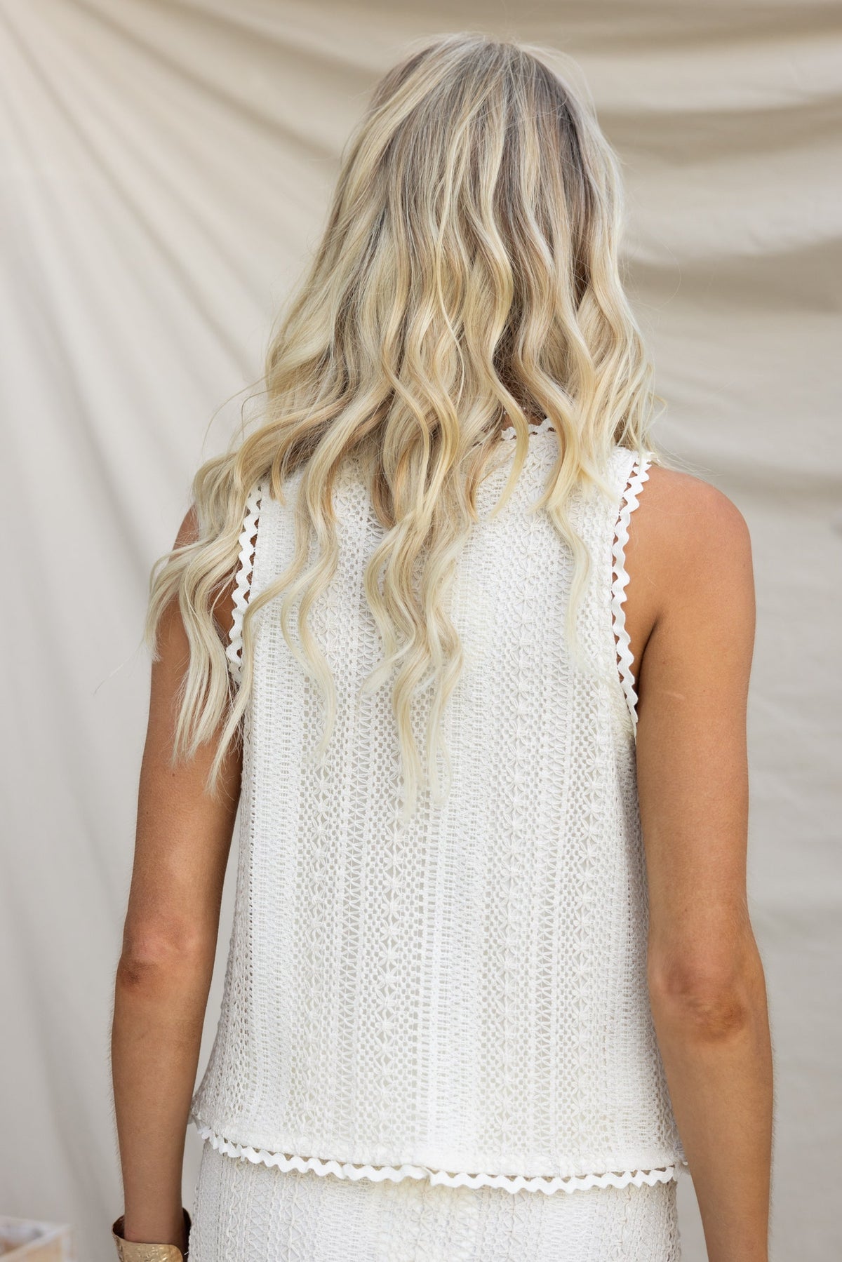 Back view of a woman wearing a white crochet top with a relaxed fit and tie detail.