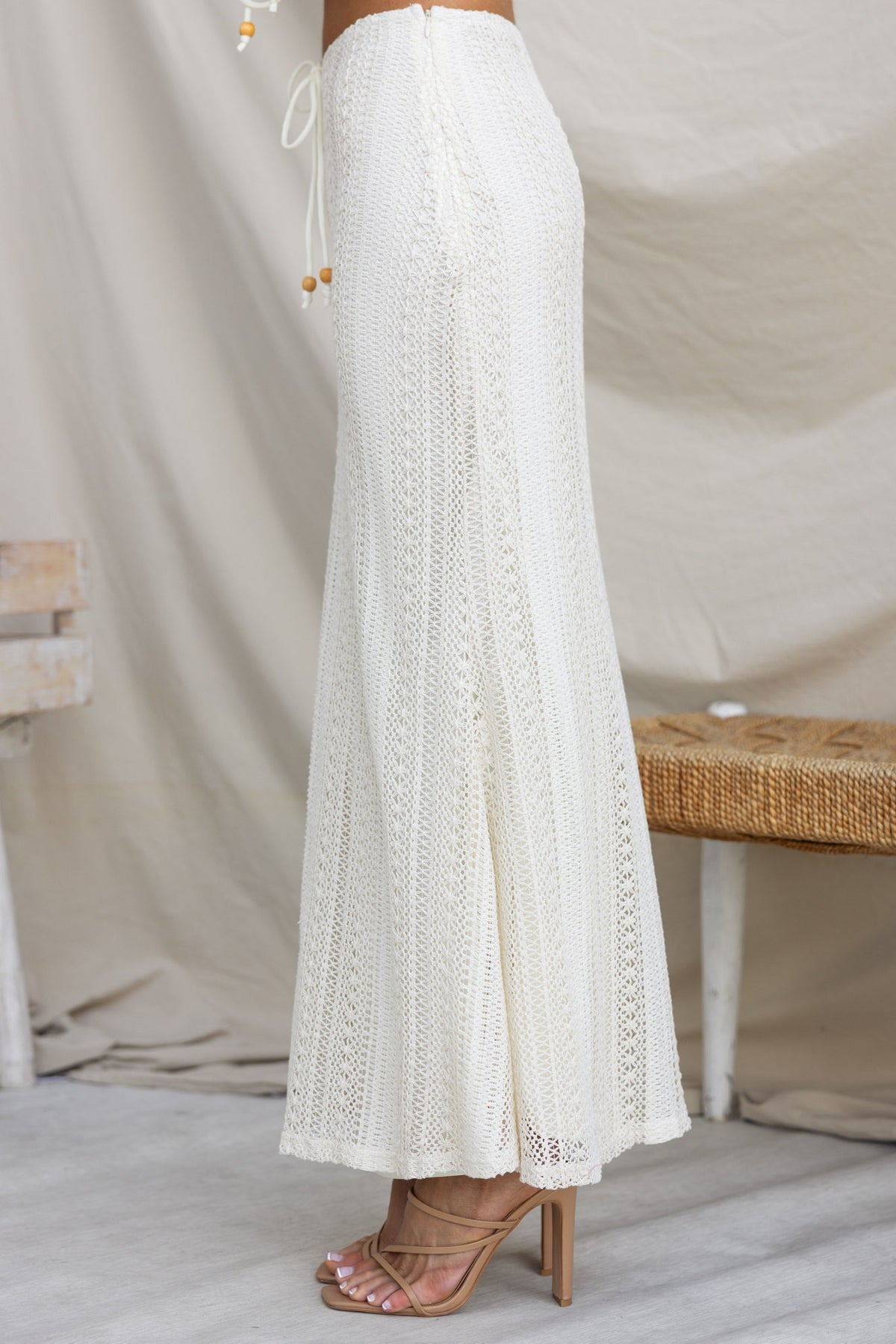 Side view of Odae Maxi Skirt in crochet material, featuring a tie detail and mid-high waist fit, styled with heels.