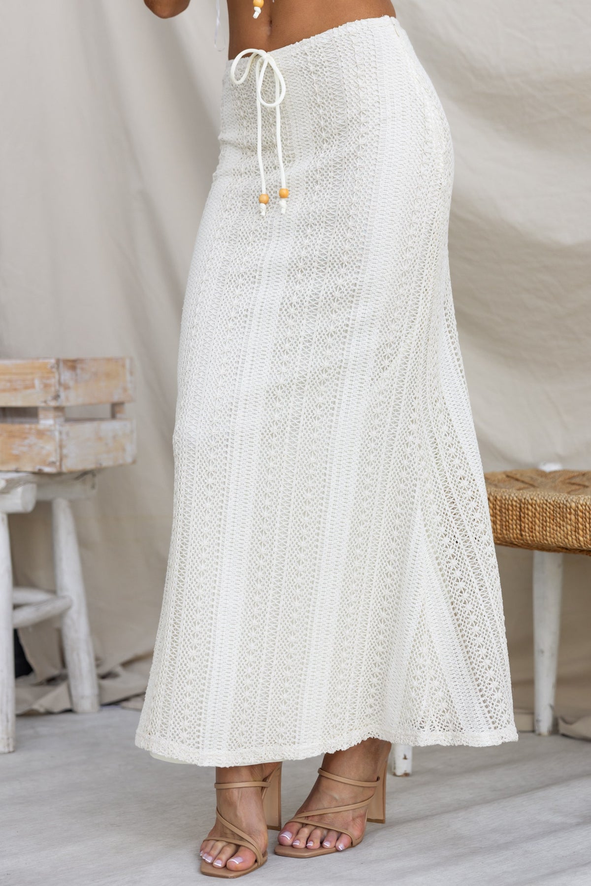White crochet maxi skirt with mid-high waist and tie detail, featuring a lined and stretchy material.