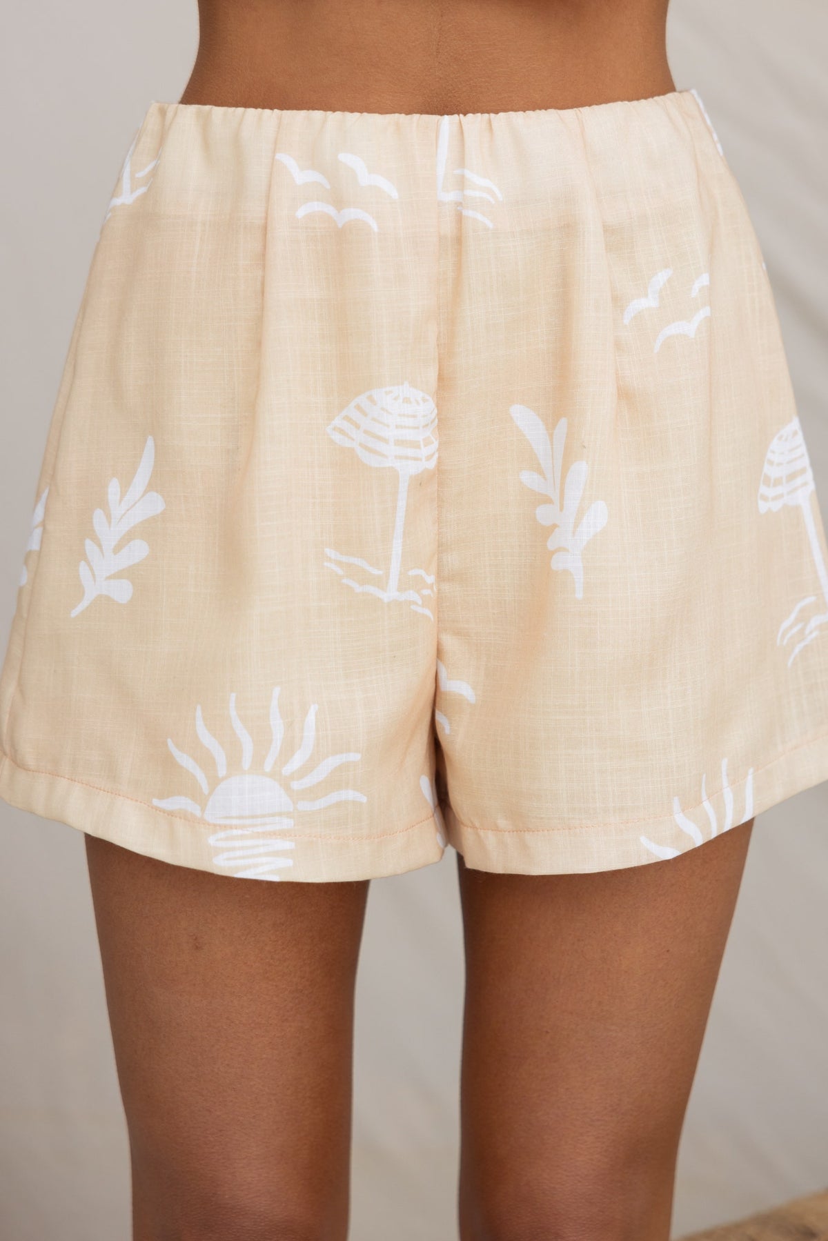 Canary Shorts featuring a light tan color with white tropical prints, mid-high waist and elastic waistband.