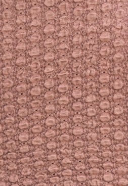 Textured fabric in soft pink color, featuring a unique raised pattern suitable for stylish apparel.