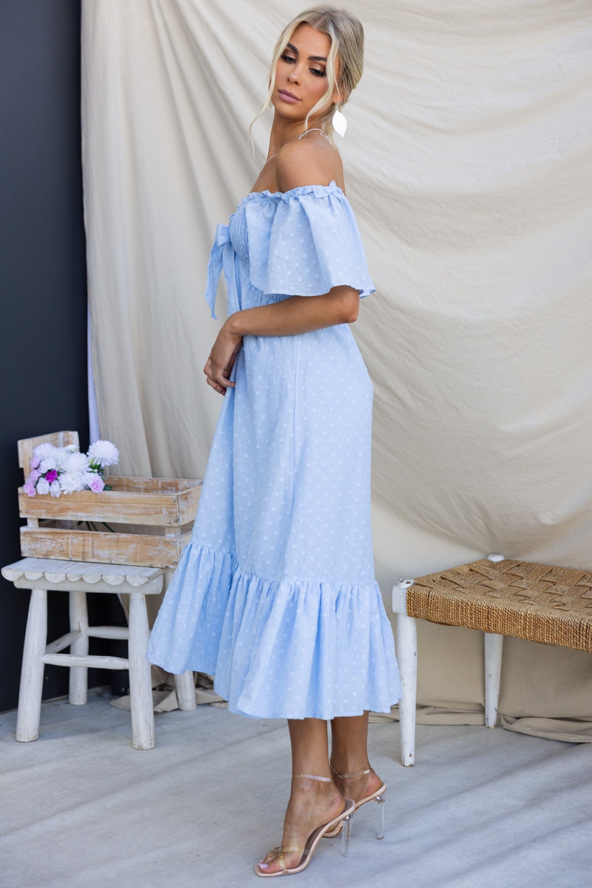 Angelis Midi Dress in light blue with off-shoulder design, textured cotton fabric, and ruffled hem, styled on model.
