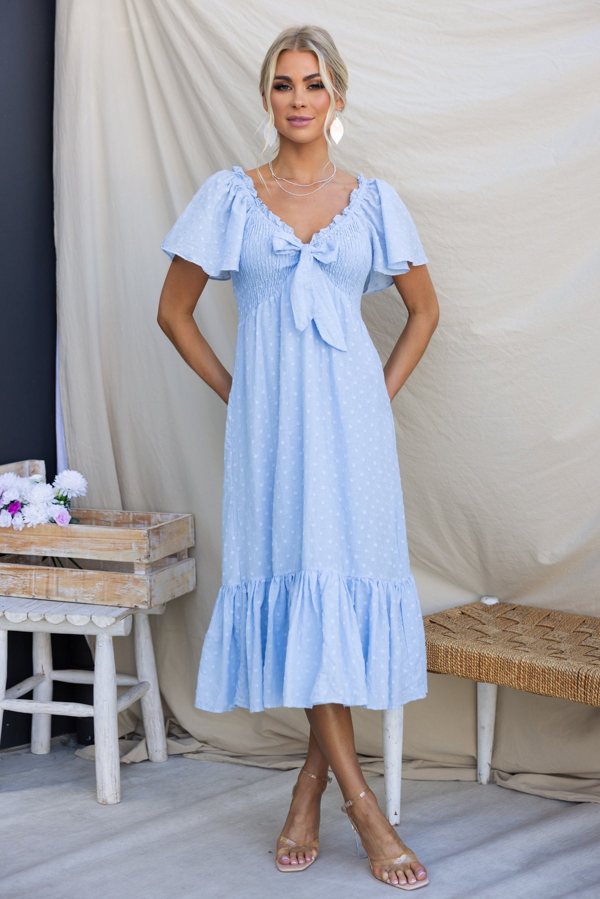 Angelis Midi Dress in light blue, featuring a bow tie at the bust, textured cotton, and flutter sleeves.
