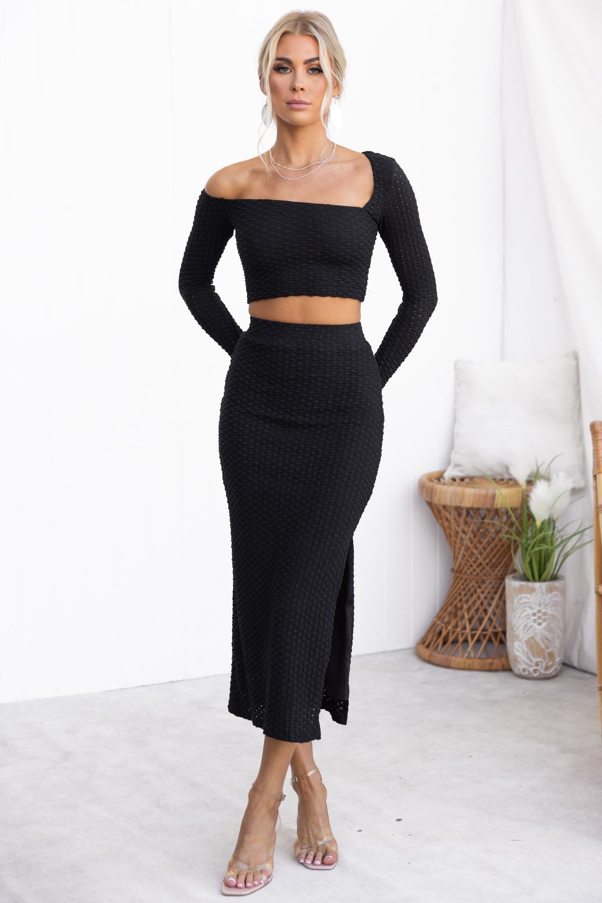 Model wearing a black Sisil Top with asymmetric neckline, paired with a matching fitted skirt, showcasing a stylish look.