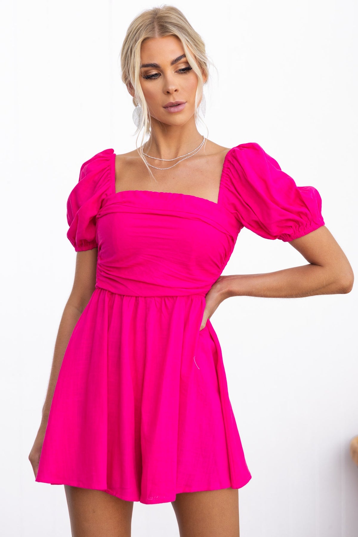 Kippy Playsuit in vibrant pink with square neckline, puff sleeves, and a flared skirt, modeled by a woman.