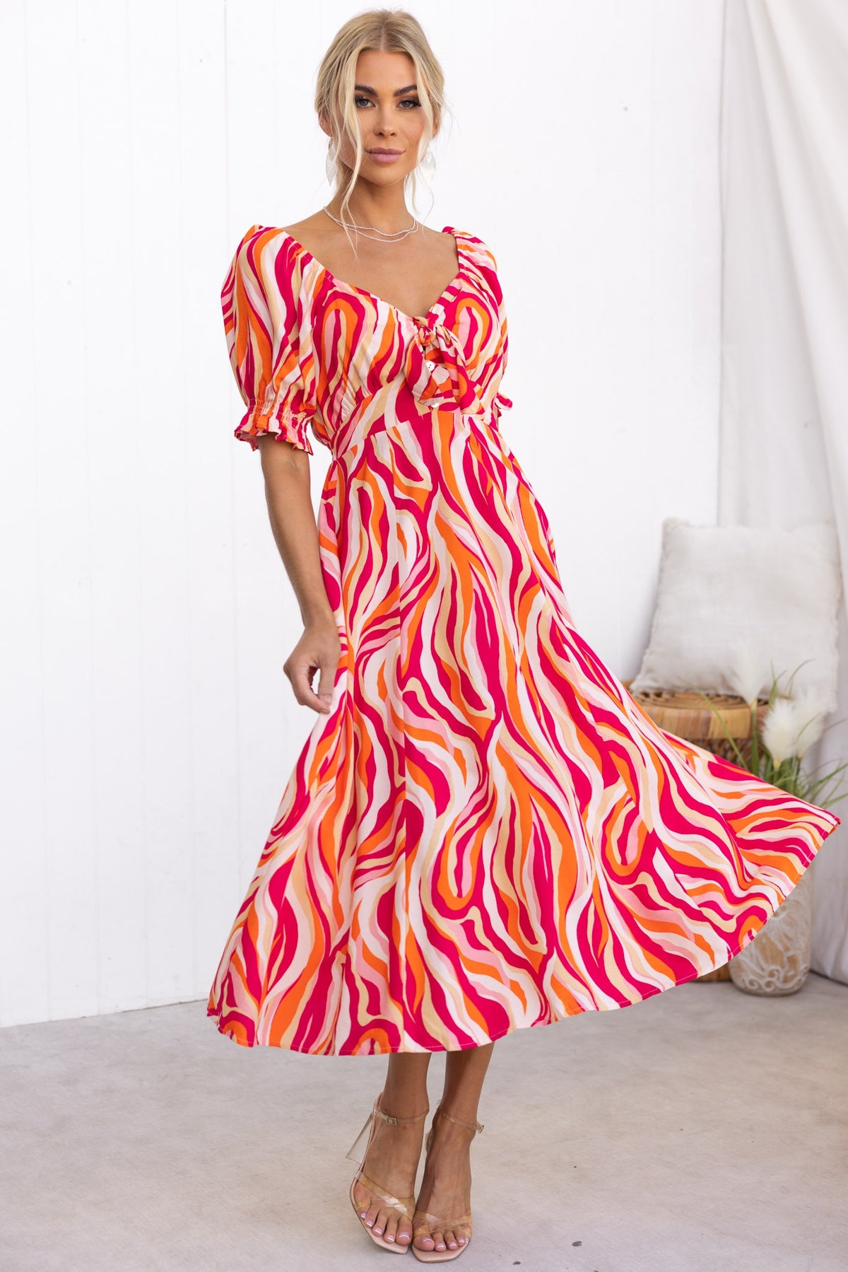 Model wearing the Rayanna Midi Dress with vibrant pink and orange swirl pattern, featuring puff sleeves and tie detail.