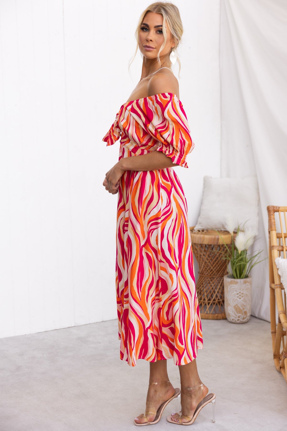 Woman wearing Rayanna Midi Dress in vibrant pink and orange wave pattern, showcasing its off-shoulder design and flowy fit.