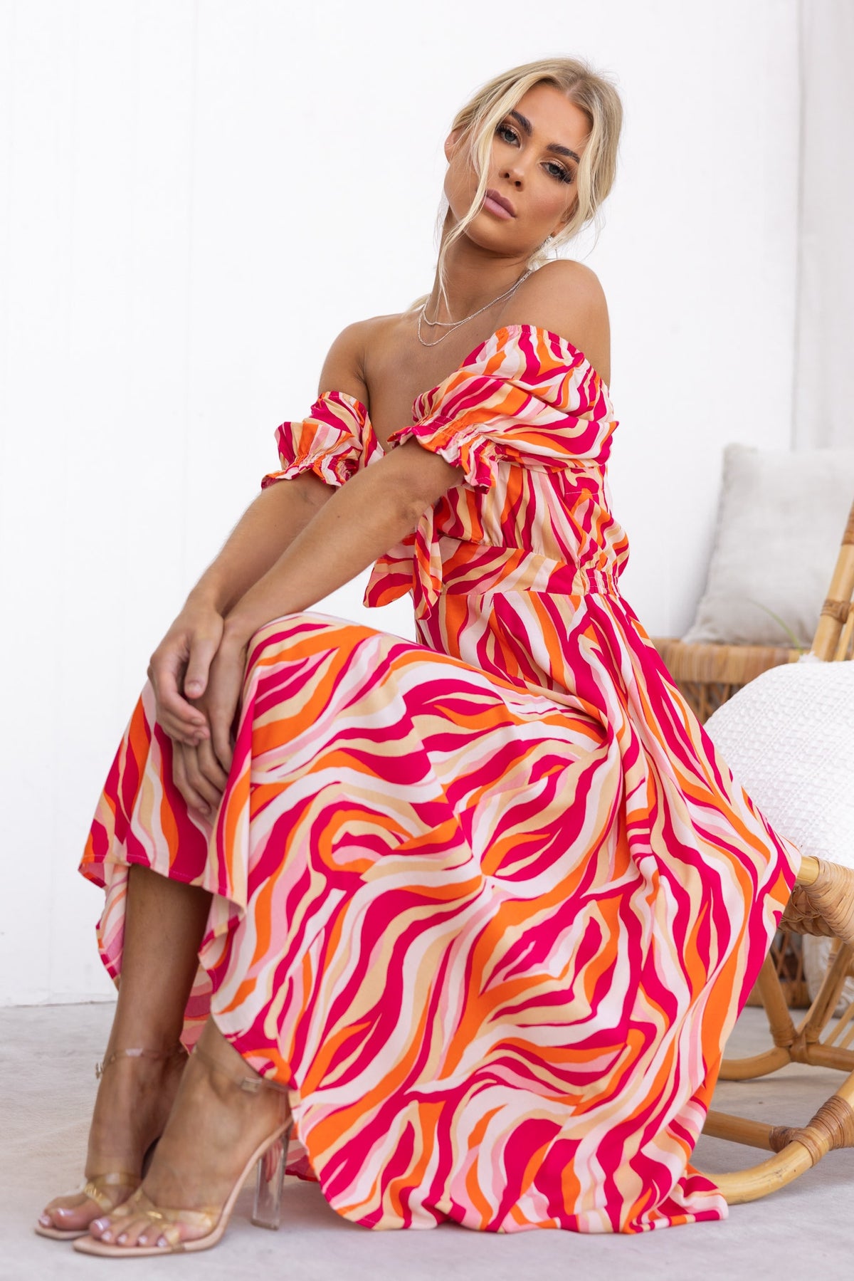 Model wearing Rayanna Midi Dress in vibrant pink and orange wavy pattern, featuring a tie bust and elastic sleeves.