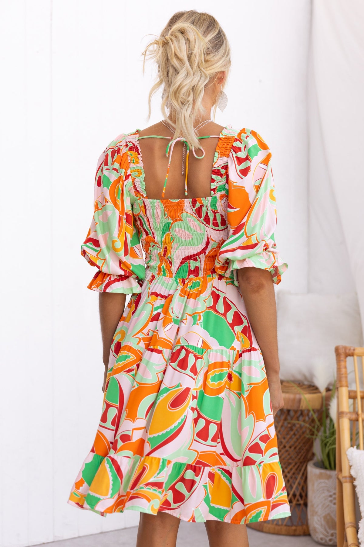 Back view of Tremmy Dress featuring an elastic bodice, colorful patterns, and puff sleeves in a flowy design.