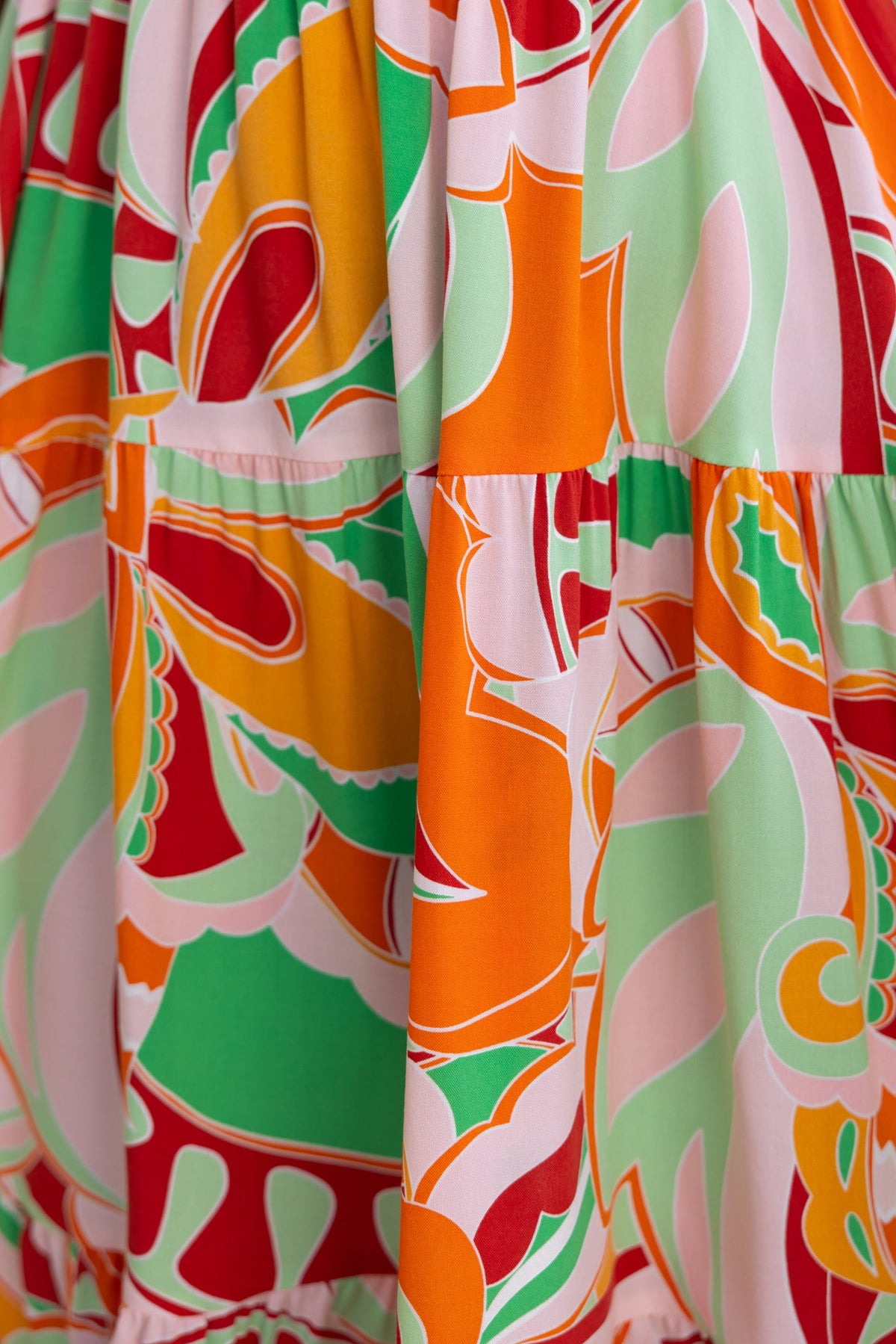 Close-up of the Tremmy Dress featuring vibrant floral print in orange, green, and pink tones on lightweight fabric.
