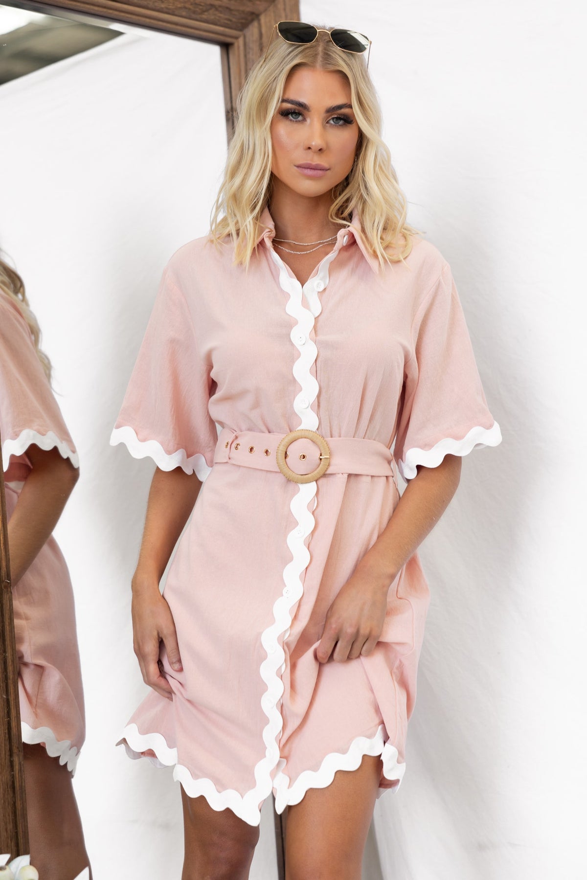 Alfonzo Dress in pink with white scalloped edges, collar, and removable belt, styled by model in a mirror reflection.