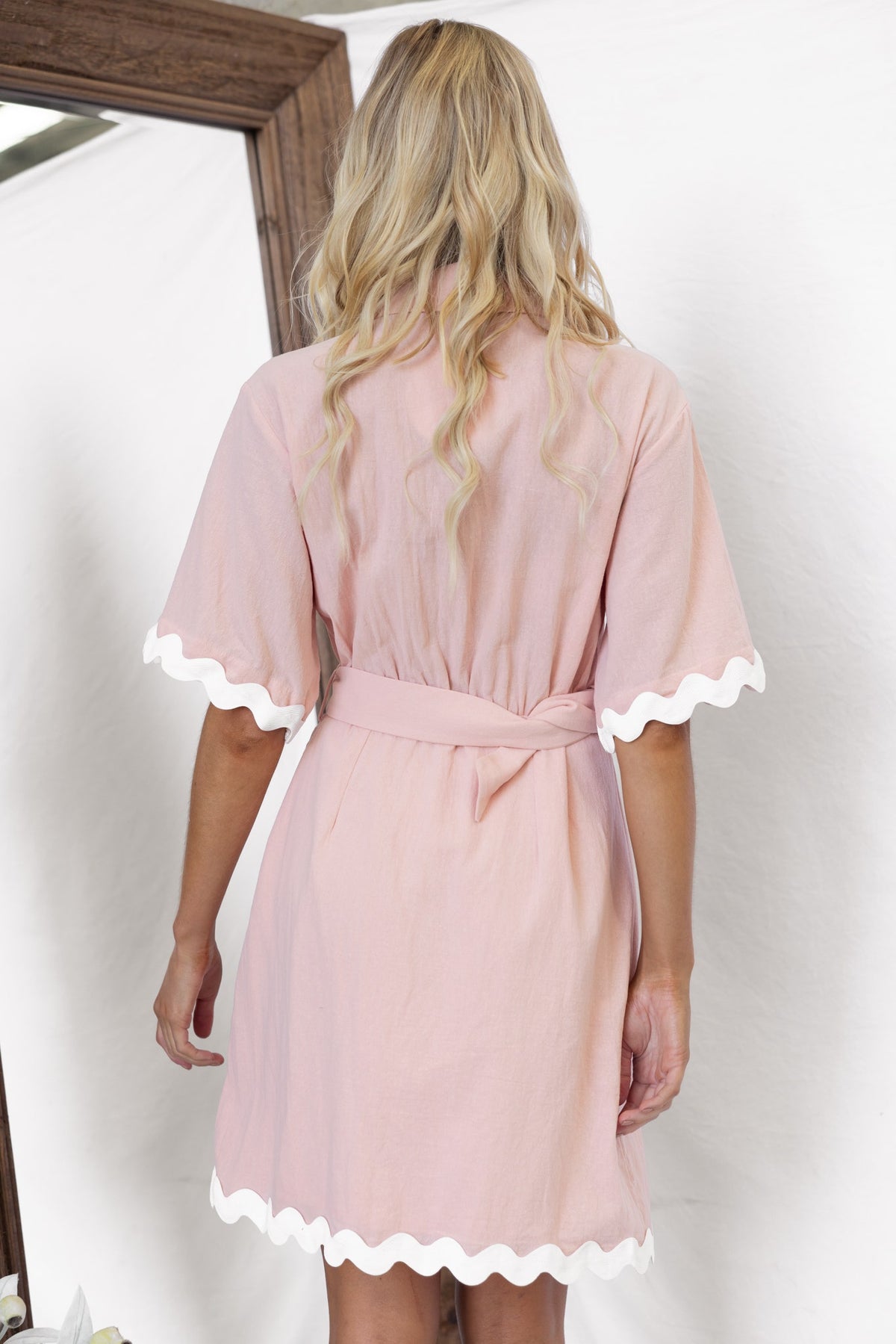 Back view of a pink Alfonzo Dress featuring scalloped edges and a removable belt, styled for a soft, elegant look.