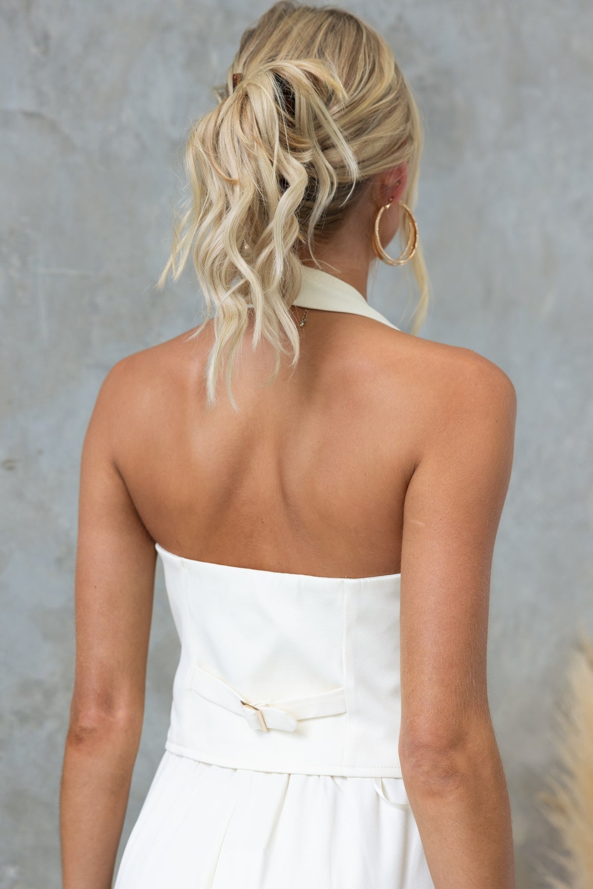 Back view of a model wearing a white Kamala Top with a halter neckline and adjustable strap.