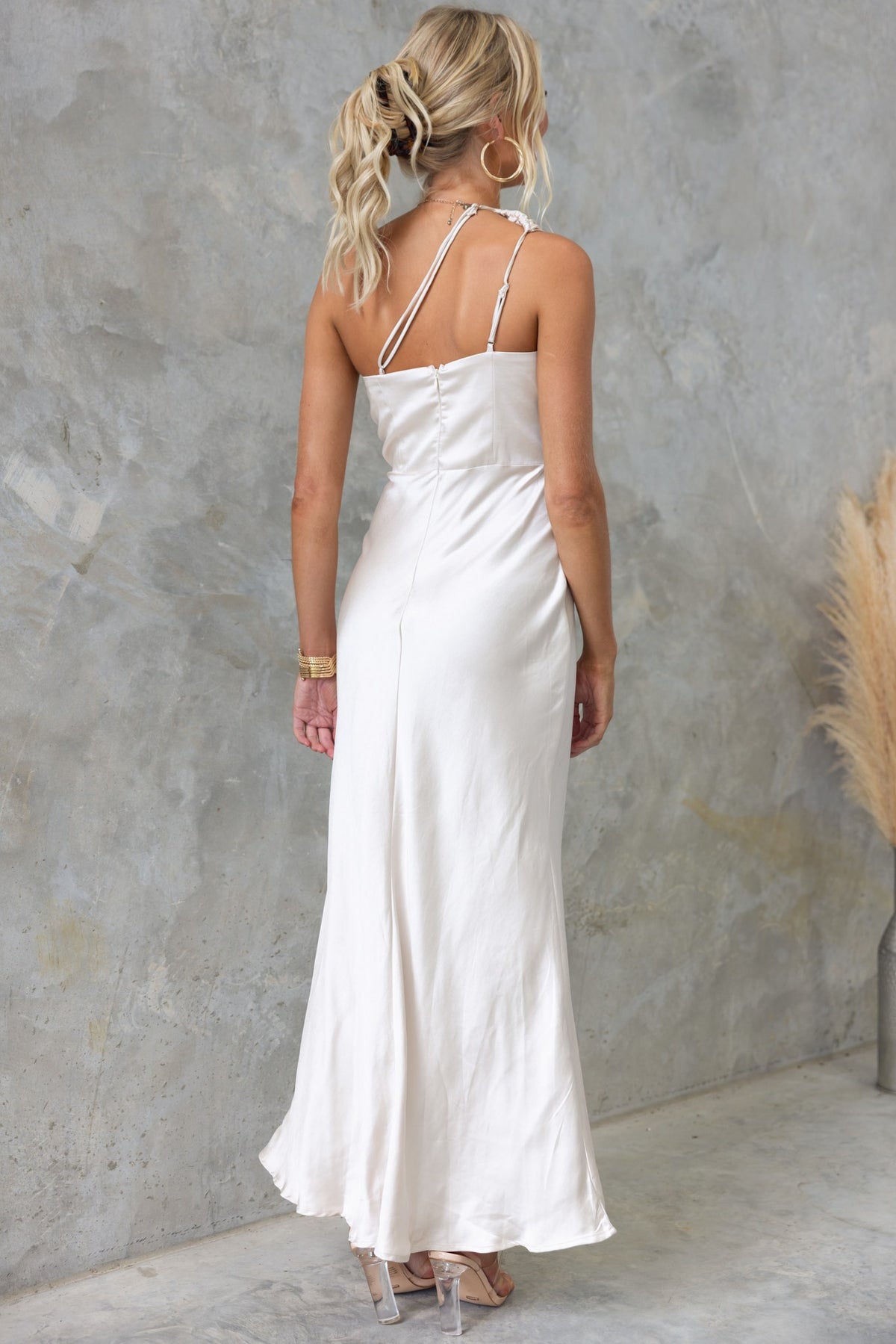 Back view of a model wearing a Bombshell Maxi Dress with adjustable straps and satin finish, featuring a split and lace detailing.