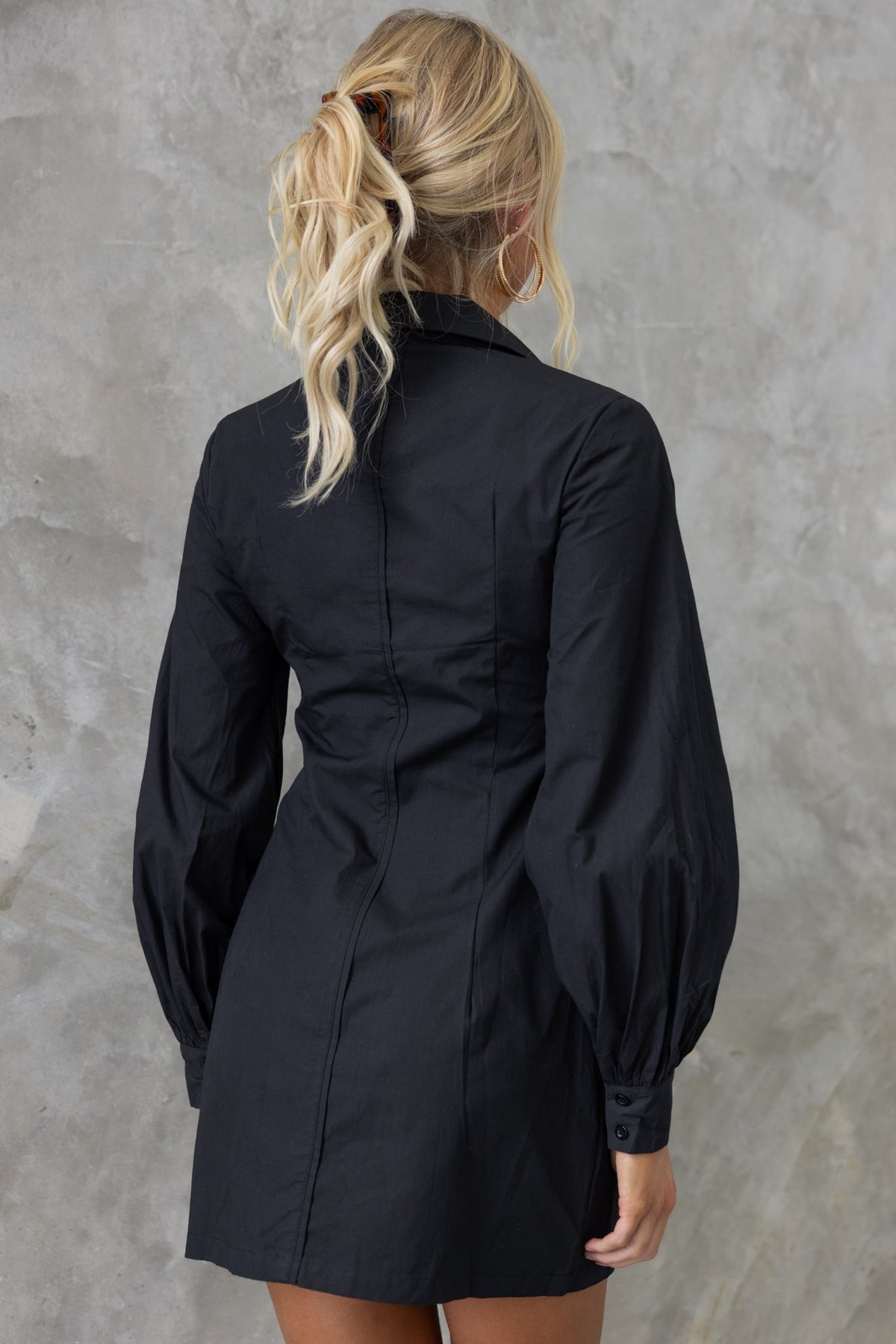 Back view of the Lanetta Dress, a black dress with a collar and puff sleeves, styled with long blonde hair.
