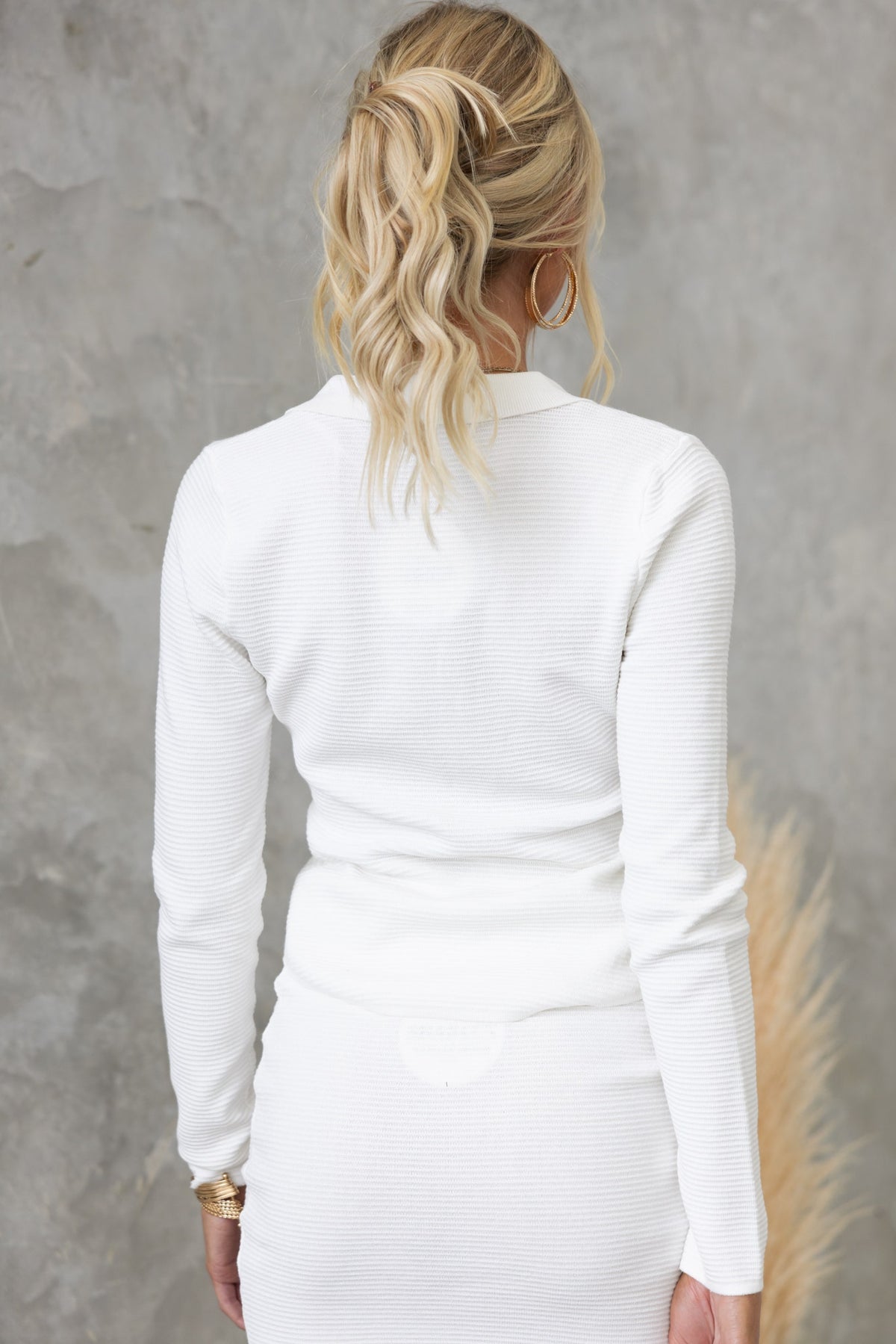 Back view of a woman wearing a white textured long-sleeve top styled with a ponytail.