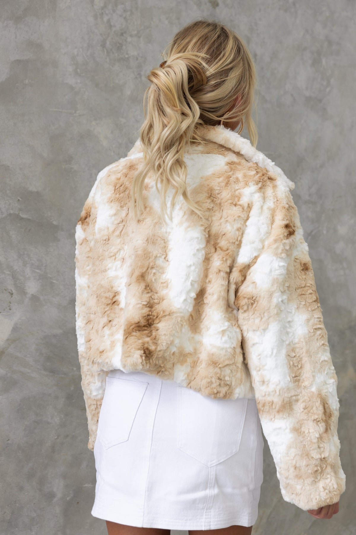 Model wearing a Florida jacket with a high neckline, soft fluffy material, shown from the back against a textured background.