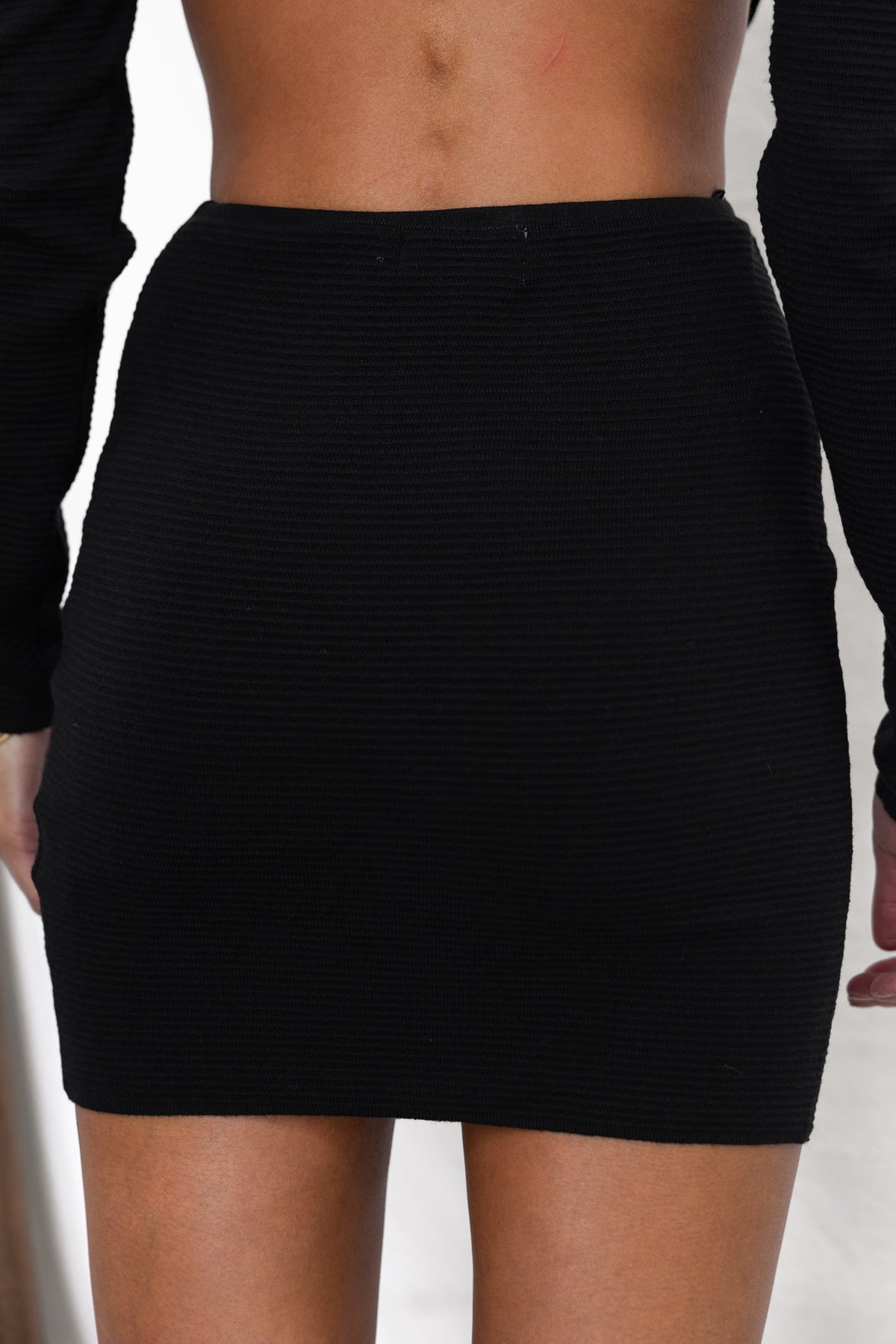 Back view of Raiza Skirt in black, showcasing its textured fabric and mid-high waist design.