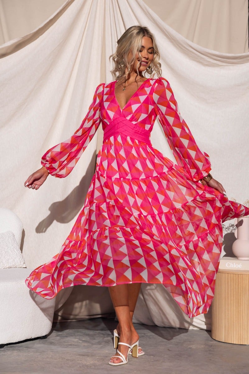 Model twirling in a multi-colour Cotta Maxi Dress featuring a V-neckline and elastic cuffs, showcasing a vibrant geometric print.