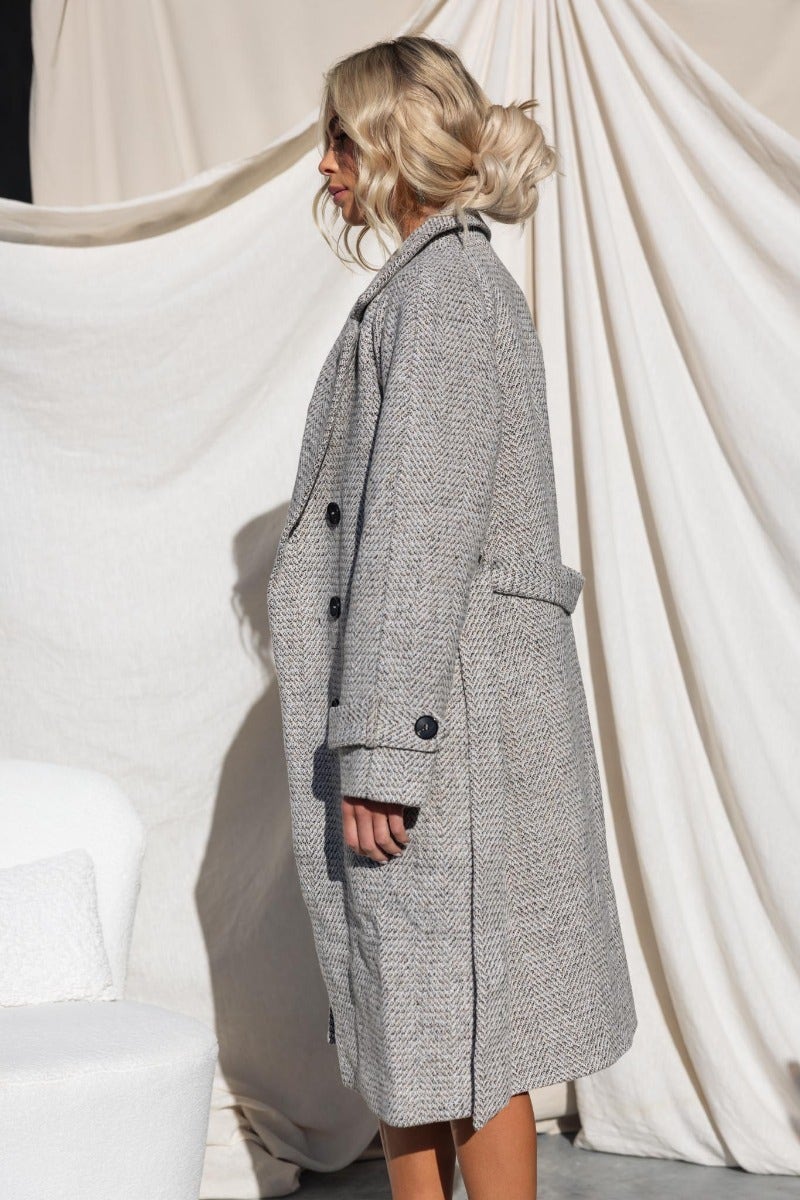 Side view of the Atthow Coat featuring a tweed look, longline fit, collar, and removable belt against a neutral backdrop.