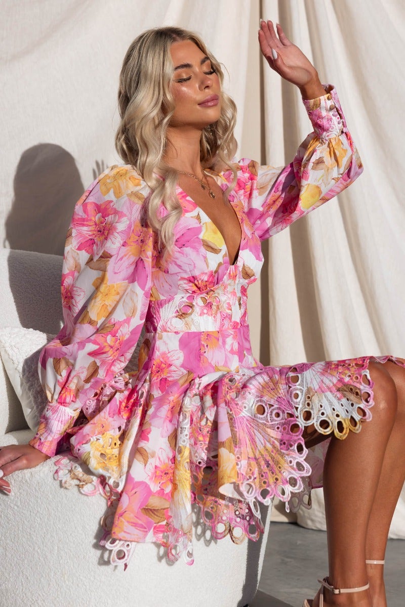 Model wearing a floral Chasing Dreams Dress with V-neckline and lace detailing in vibrant pink hues.