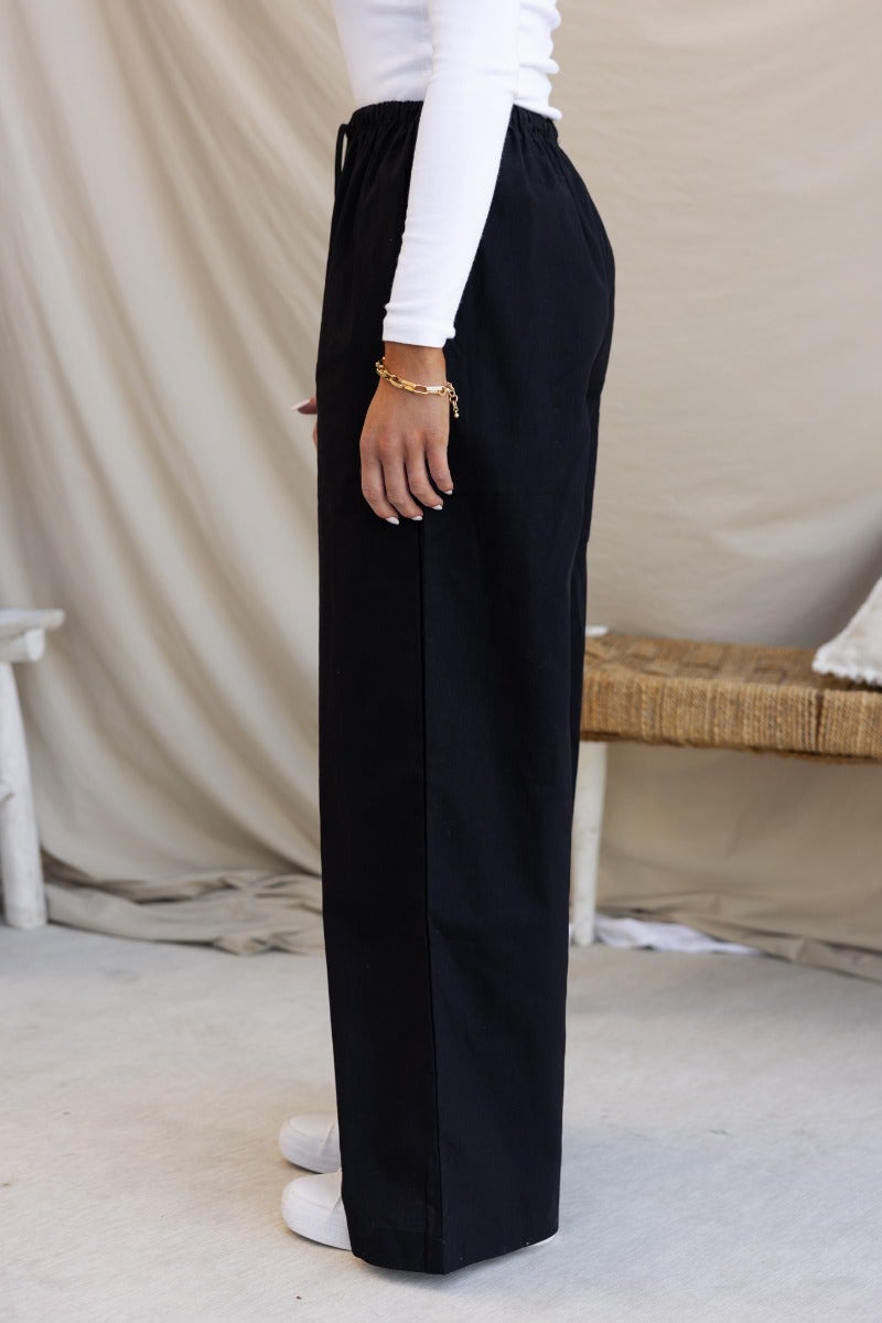 Side view of black cotton Peru pants with elastic waistband and wide legs, shown on model.