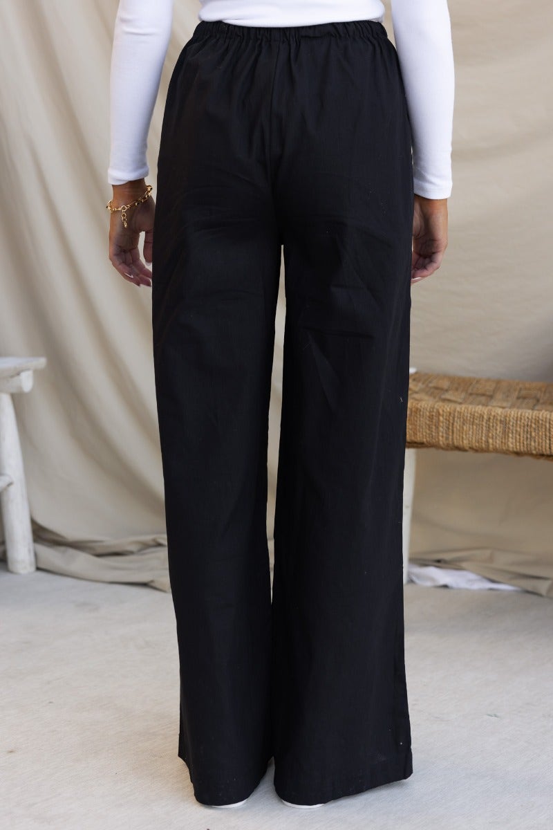 Black wide-leg cotton pants with elastic waistband and drawstring, shown from the back.