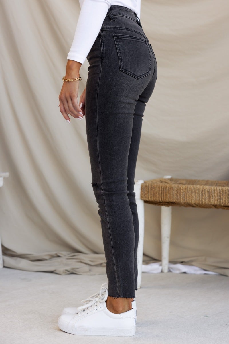 Profile view of Dion Jeans in washed black denim with a mid-high waist fit and distressed rips, styled with white sneakers.