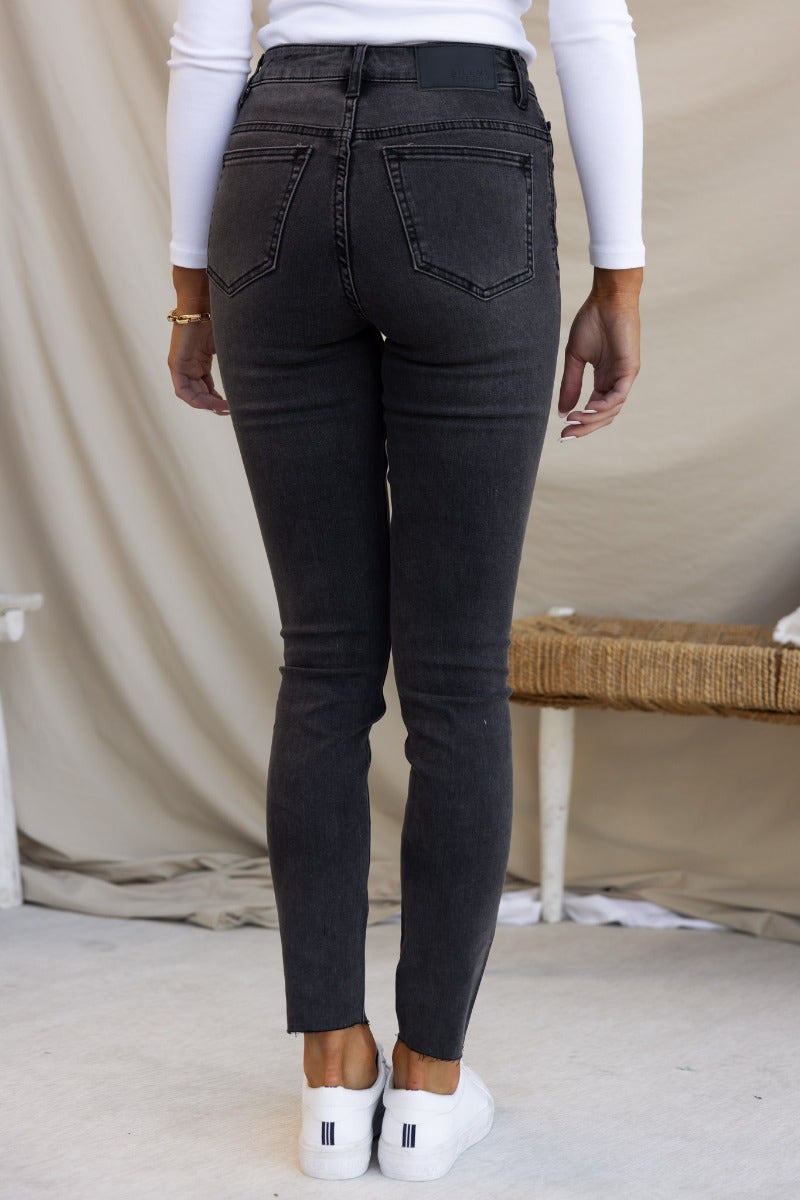 Woman wearing Dion Jeans, washed black denim, mid-high waist, skinny fit with distressed rips and raw hemline.