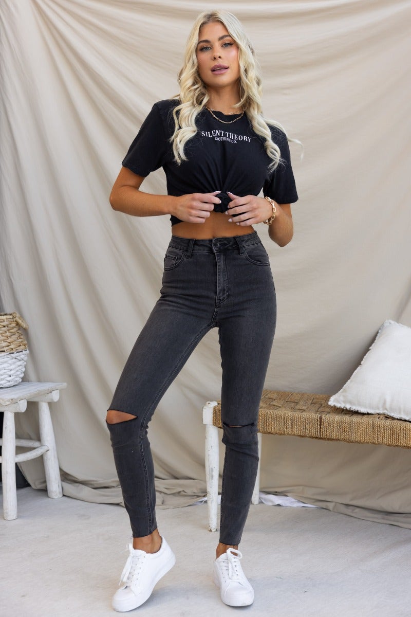 Model wearing Dion Jeans in washed black denim, featuring mid-high waist, distressed rips, and raw hemline.