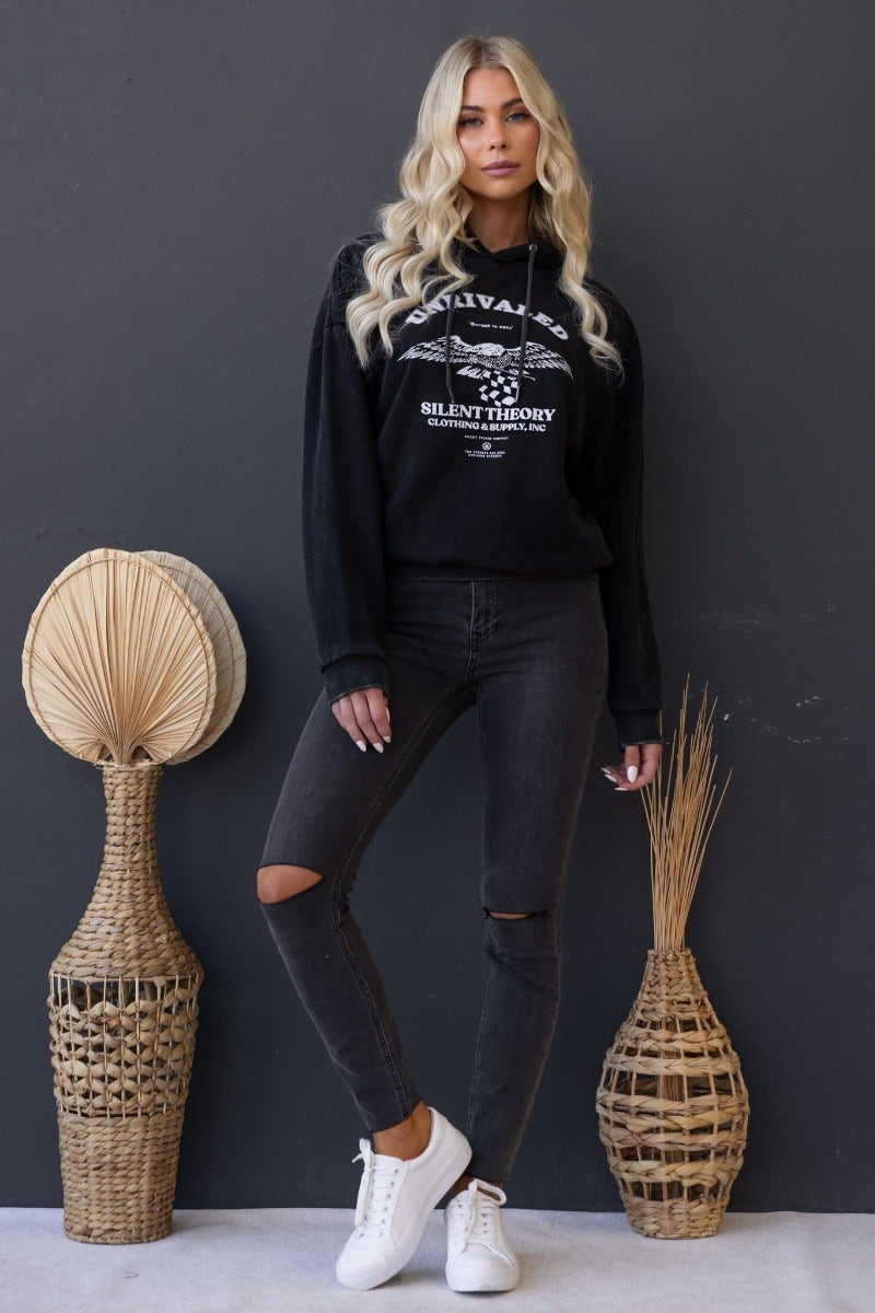 Model wearing Ivar Jumper in washed black with 'Unrivaled' print, paired with ripped jeans and white sneakers.