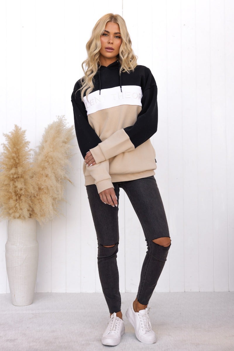 Model wearing Nayle Jumper, a black and beige oversized hoodie, paired with ripped jeans and white sneakers.