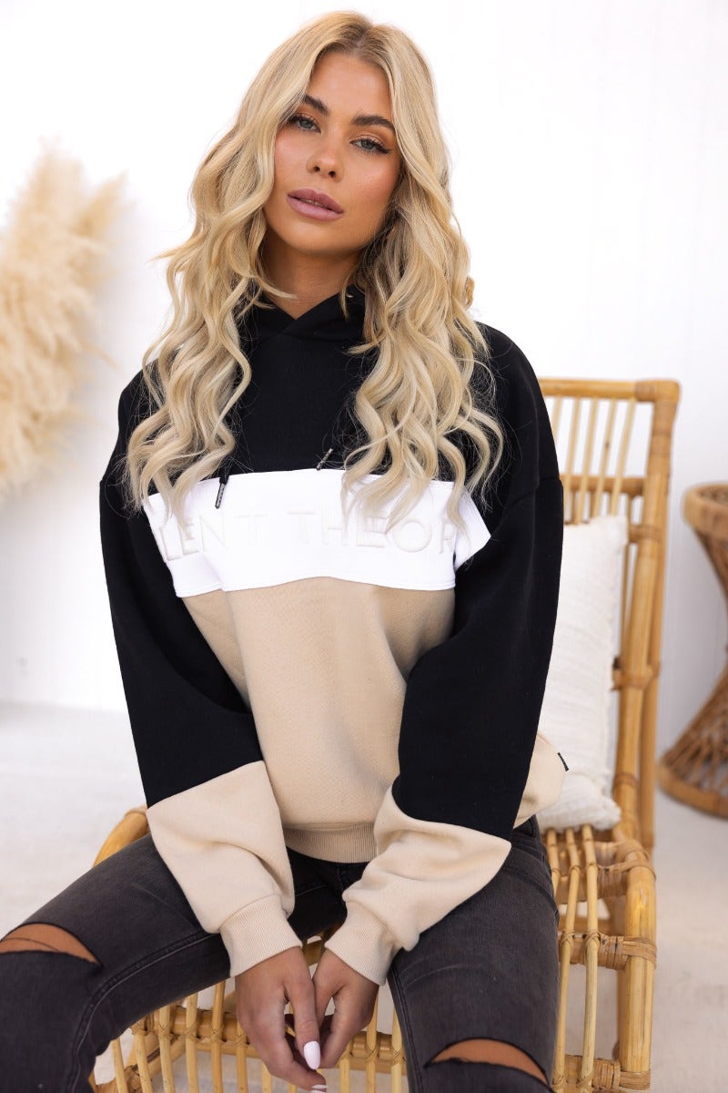 Nayle Jumper by Silent Theory featuring a black and beige design with hood, worn by model in stylish setting.