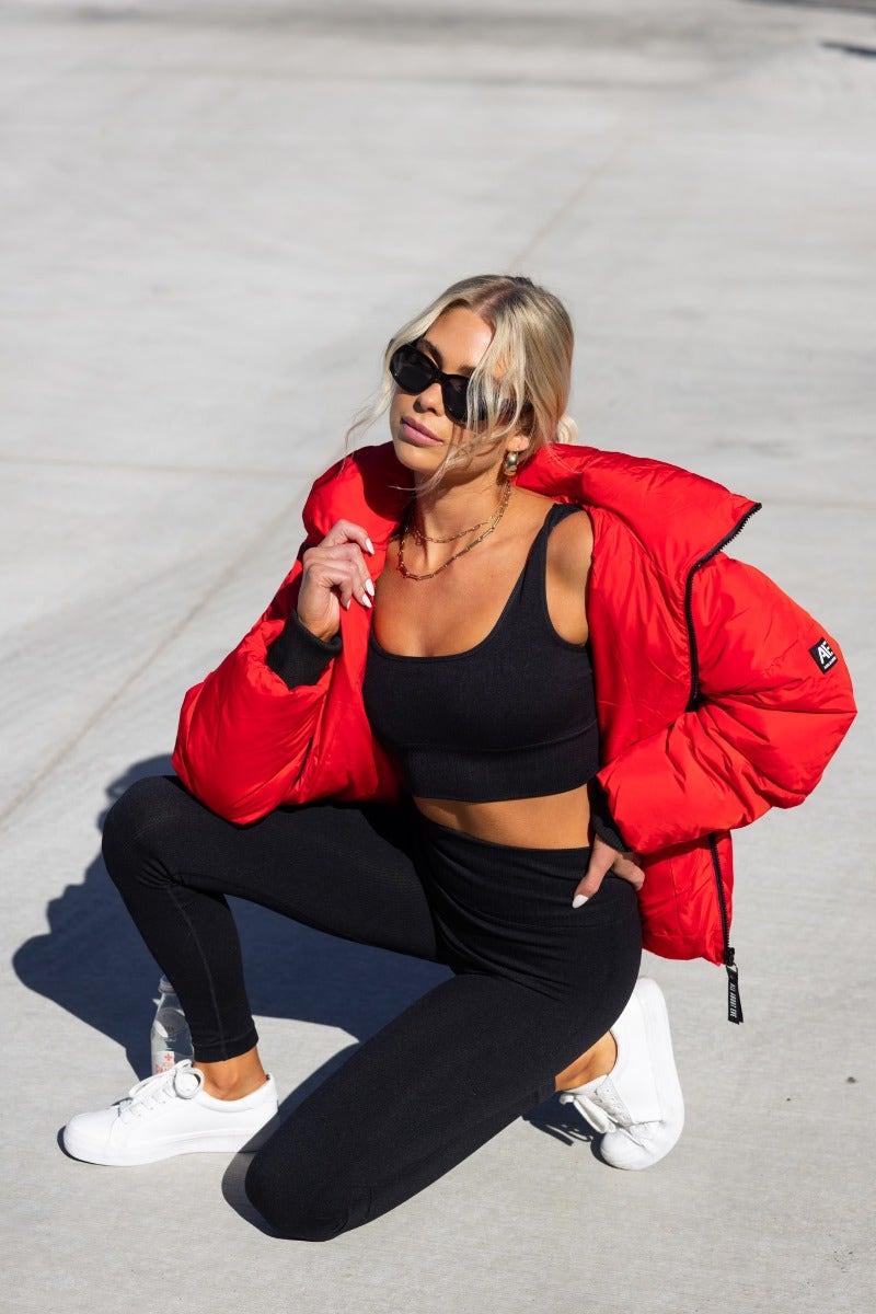 Delila Puffer Jacket in red worn by model, featuring high neckline, zip-up front, and removable hood.