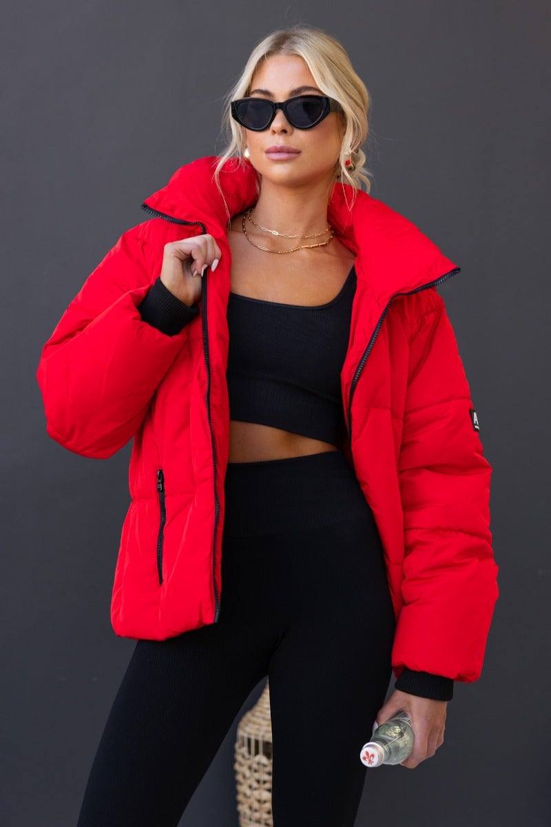 Model wearing Delila Puffer Jacket in red with high neckline, removable hood, and zip-up front.